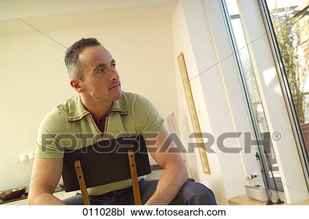 Young man sitting on chair and looking out of window View Large Photo Image Stock Image - Young man sitting on chair and looking out of window. Fotosearch