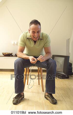 Young man sitting on chair laughing heartily View Large Photo Image Stock Image - Young man sitting on chair laughing heartily. Fotosearch