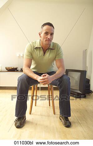 Young man sitting on chair with sceptical expression View Large Photo Image Stock Image - Young man sitting on chair with sceptical expression. Fotosearch