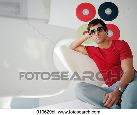 young man wearing sunglasses sitting in stylish furniture View Large Photo Image Stock Image - young man wearing sunglasses sitting in stylish furniture. Fotosearch