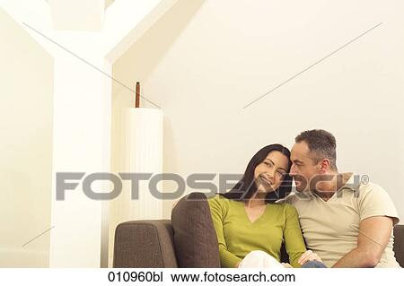 Stock Image - Young smiling couple sitting on sofa. Fotosearch