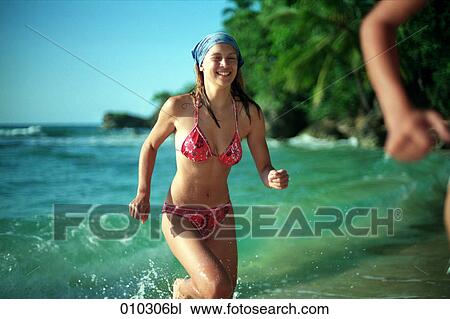 Stock Image - young teenage woman (16-19 years) running out of the water. Fotosearch