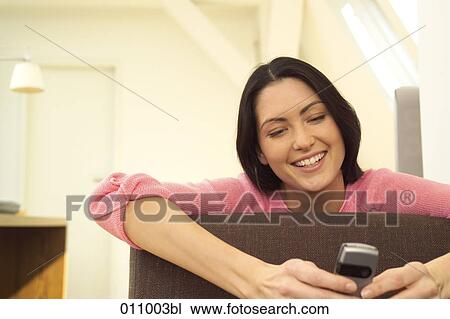 Young woman leaning over armrest of couch writing text messages on mobile View Large Photo Image Stock Image - Young woman leaning over armrest of couch writing text messages on mobile. Fotosearch