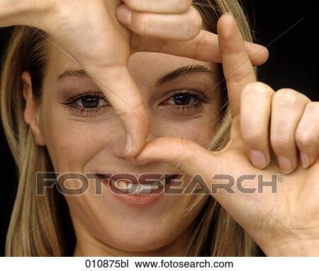 Stock Image - Young woman looking through her fingers. Fotosearch