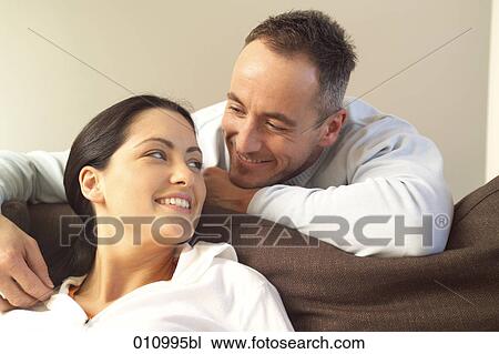 Stock Image - Young woman on sofa leaning back to her partner. Fotosearch