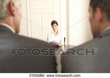 Stock Image - young woman sitting at a conference table with two businessmen in the foreground. Fotosearch
