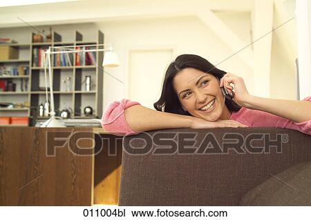 Young woman talking on mobile in her living room View Large Photo Image Stock Image - Young woman talking on mobile in her living room. Fotosearch