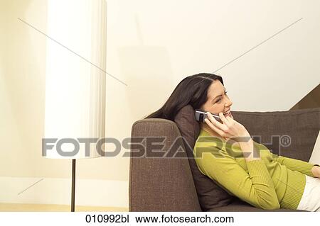 Young woman talking on mobile phone while lying on the sofa View Large Photo Image Stock Image - Young woman talking on mobile phone while lying on the sofa. Fotosearch