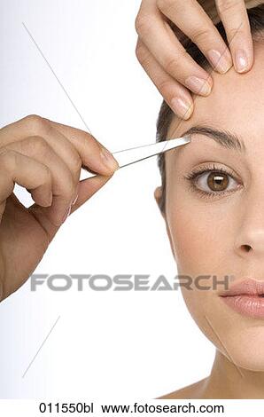 Stock Image - a young woman plucking her eyebrows. Fotosearch