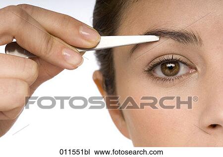 Stock Image - a young woman plucking her eyebrows with tweezers. Fotosearch
