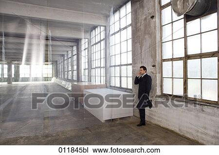 Stock Image - businessman in dark suit standing in empty factory building and talking on mobile. Fotosearch