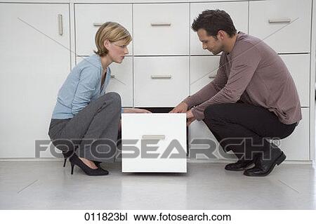 Stock Image - female and male office worker together at filing cabinet. Fotosearch