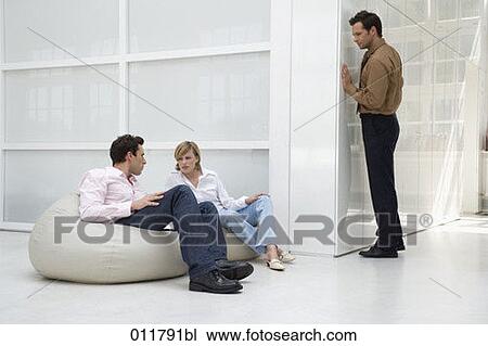Stock Image - man peeping around the corner to listen to conversation between a man and woman. Fotosearch