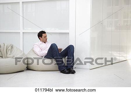 Stock Image - man sitting on bean bag using mobile phone. Fotosearch