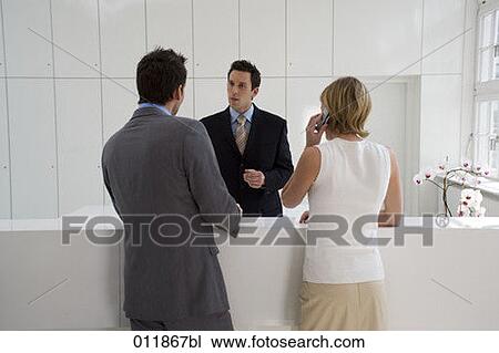 Stock Image - receptionist talking to businessman while woman is answering her mobile. Fotosearch