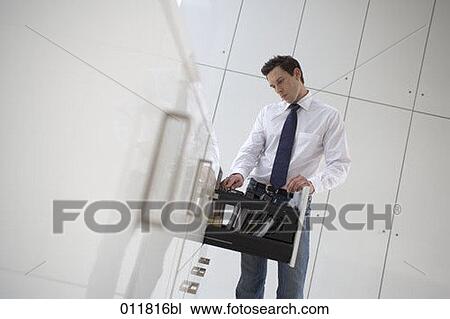 Stock Image - sceptical looking businessman at filing cabinet. Fotosearch