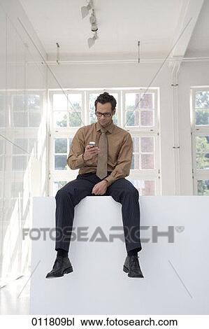 Stock Image - sitting young businessman looking at display of his mobile. Fotosearch