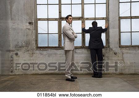 Stock Image - two businessmen standing in empty factory building one looking ot of window. Fotosearch