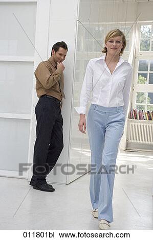 Stock Image - young grinning man looking after woman passing by in office building. Fotosearch