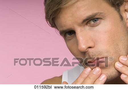 Stock Image - young man checking his skin in a mirror. Fotosearch