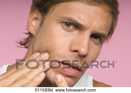 Stock Image - young man checking his skin in a mirror. Fotosearch