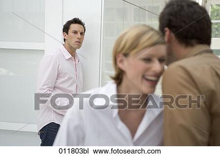 Stock Image - young man looking suspiciously at laughing couple. Fotosearch