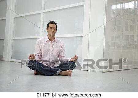 Stock Image - young man sitting on the floor meditating. Fotosearch