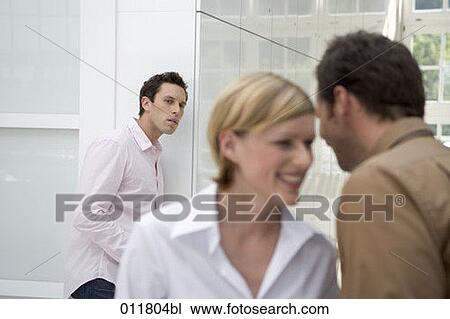 Stock Image - young office worker looking suspiciously at laughing colleagues . Fotosearch