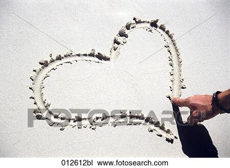 Stock Image - close-up of man drawing a the shape of a heart in the sand. Fotosearch