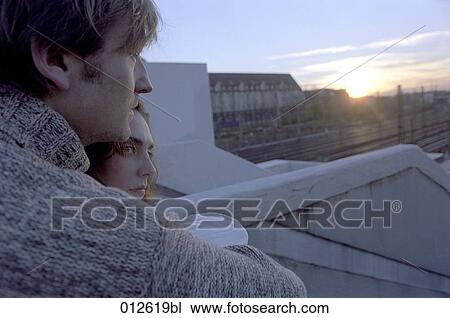 close-up of young couple standing on bridge looking into the sunset with woman looking worried View Large Photo Image Stock Image - close-up of young couple standing on bridge looking into the sunset with woman looking worried. Fotosearch