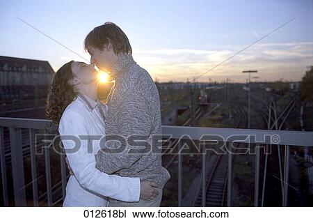 Stock Image - couple about to kiss on bridge in sunset. Fotosearch