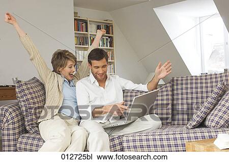 couple sitting on sofa with laptop celebrating View Large Photo Image Stock Image - couple sitting on sofa with laptop celebrating. Fotosearch