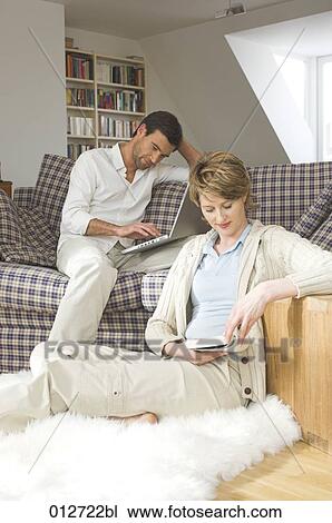 couple sitting together in living room woman reading and man working with computer View Large Photo Image Stock Image - couple sitting together in living room woman reading and man working with computer. Fotosearch