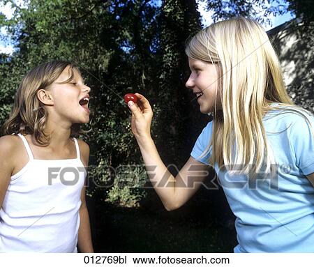 Stock Image - little girl feeding friend with cherry. Fotosearch