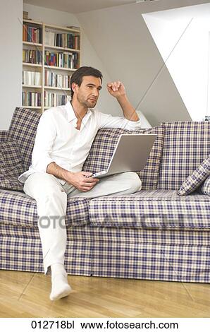 man with laptop on his knees sitting on sofa thinking View Large Photo Image Stock Image - man with laptop on his knees sitting on sofa thinking. Fotosearch