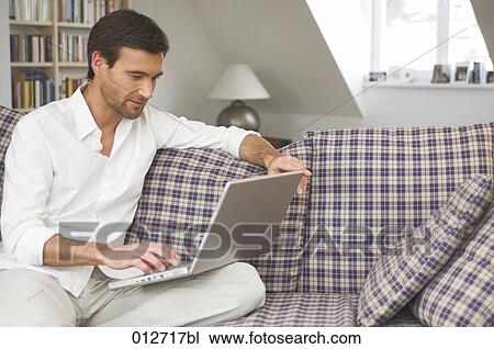 Stock Image - mature man sitting comfortably on sofa working with his laptop. Fotosearch