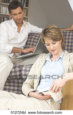 Stock Image - mature man watching his wife reading a book. Fotosearch