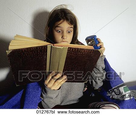 Stock Image - portrait of astonished looking girl reading book at night. Fotosearch