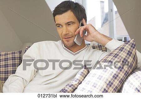 Stock Image - portrait of man in his living room talking on cellular phone. Fotosearch