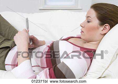 Stock Image - portrait of teenage girl lying on sofa with her cellphone. Fotosearch