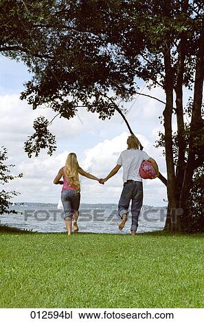 Stock Image - rear view of young couple walking hand in hand. Fotosearch