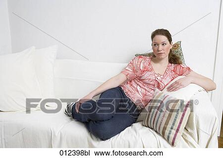 Stock Image - thoughtful looking young woman sitting on couch. Fotosearch
