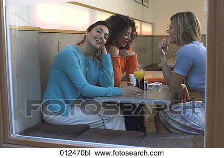 Stock Image - three young women talking in cafe one looking out of the window. Fotosearch