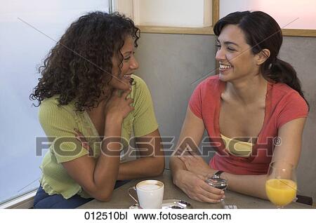 Stock Image - two women friends smiling at each other in cafe. Fotosearch