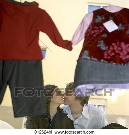 Stock Image - view through window of shop with baby clothes at couple sharing a kiss. Fotosearch
