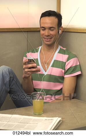 Stock Image - young man looking at his ipod in restaurant. Fotosearch