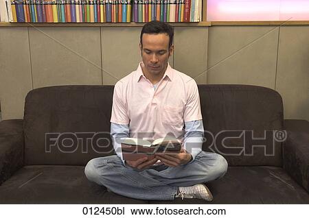 young man sitting on couch reading book View Large Photo Image Stock Image - young man sitting on couch reading book. Fotosearch
