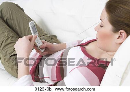 young woman lying on sofa looking at display of her mobile View Large Photo Image Stock Image - young woman lying on sofa looking at display of her mobile. Fotosearch
