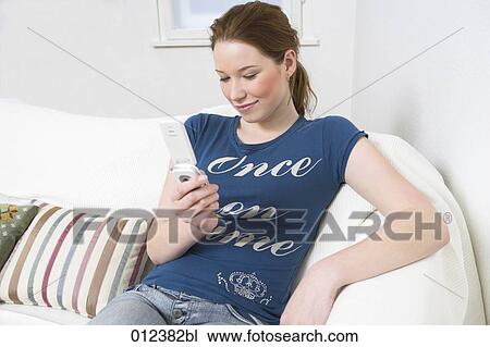 young woman sitting on sofa reading text messages on her mobile View Large Photo Image Stock Image - young woman sitting on sofa reading text messages on her mobile. Fotosearch