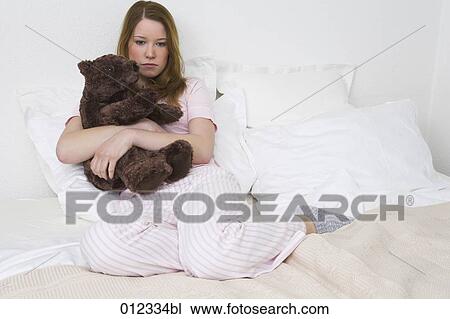 young woman with thoughtful expression sitting on bed holding cuddly toy View Large Photo Image Stock Image - young woman with thoughtful expression sitting on bed holding cuddly toy. Fotosearch